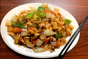 A plate of Black Bean Chicken with chicken, bell peppers, onions, and carrots in black bean sauce, served with chopsticks on a wooden table at Chopsticks，a Chinese Restaurant in Kent